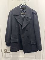 Front view of black double-breasted pea coat on hanger showing pockets, collar, buttons