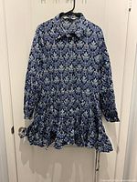 Front view of blue patterned Zara dress hanging, showing collar, buttons, ruffled hem