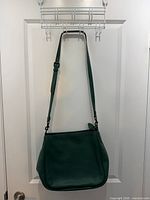 Front view of dark green Coach leather bag hanging from strap