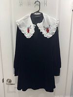 Front view of black velour dress showing white ruffled collar with heart and sword embroidery.