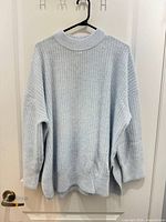 Front view of light-blue H&M rib-knit sweater showing mock neck, drop shoulders, side slits