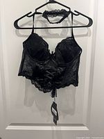 Front view of black velour/lace bralette on hanger with lace neck strap, tags visible