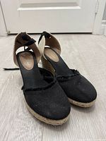 Front view of black canvas wedge espadrilles showing uppers, ankle ties, jute wedge platforms