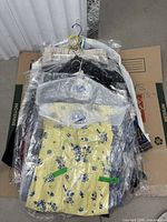 Stack of approximately 10 dresses on hangers in plastic coverings