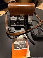 Camera, flash, case, lens cap, strap, manual and pouch laid out on surface