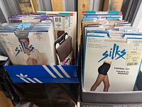 Two boxes filled with sealed pantyhose packages from Silks, Jockey, Dim