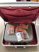 Open suitcase showing burgundy lining, nested train case and packaged keychains