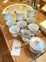 Full grouping of ten cups, creamer and covered sugar bowl showing pattern and trim