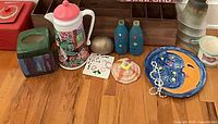 Group shot of decor items including wood organizer, painted bottles, pitcher, tissue box cover, ceramic pieces, necklace, tiles, metal sphere and license plate frame