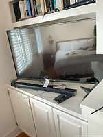 Front view of LG 49-inch TV on cabinet with soundbar and remotes