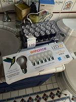 Box of Enhance LED60 bulbs, clear organizer, additional items visible