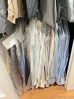 Closet section with approximately 15 dress shirts on hangers, various colors, some in garment bags