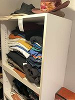 Full shelving unit showing stacked clothing and two hats