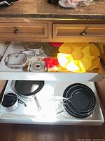Drawer showing assorted bakeware and serveware items including CorningWare casserole, white baking dishes, yellow segmented platter, red trivet