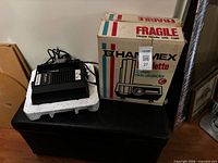 Projector on foam base beside original Hanimex box