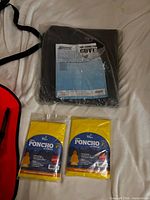 Overall lot view showing Brinmar AC cover in bag and two sealed vinyl ponchos