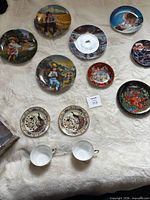 Group shot of all ten decorative plates, two teacups visible