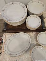 Stacked dinner plates, salad plates and bowls on wooden stand with oval platter and additional bowls visible