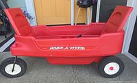 Side view of red Radio Flyer plastic wagon showing logo, seats and wheels