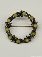 Front view of round sterling brooch with green cabochons and marcasites