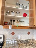 cabinet shelves showing assorted glass storage jars with metal lids and acrylic bin plus countertop spice rack