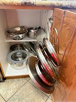 Cabinet interior showing pots, colanders, steamer insert, and multiple lids on rack