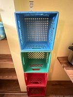 Stack of four colored plastic milk crates showing colors and overall condition