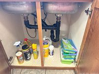 Under-sink view showing multiple cleaning bottles, wipes tub, aerosol can and cleanser can