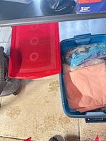 Red and blue storage totes on floor, blue tote contains folded peach fabric and bagged notions