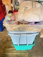 Stacked plastic bins with clear top bin containing yarn and trims, larger blue and green totes below