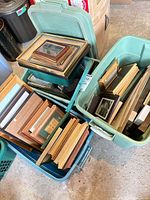 Two teal plastic totes filled with assorted picture frames of different sizes and finishes