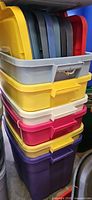 Stack of four coloured plastic totes with multiple lids visible