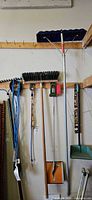 Group of hanging tools: extension cord, push broom, roof rake handle, utility brush