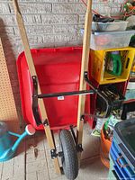 Full front view of wheelbarrow showing red tray, wooden handles, black metal frame