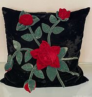 Front view of black velvet pillow with three red velvet roses and green leaves