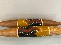Two painted wooden clap sticks side by side showing central painted motif