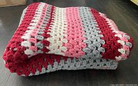 Folded crochet blanket showing striped granny square pattern in red, pink, white, grey