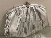 Front view showing silver metallic clutch, gathered body, chain strap, kiss-lock clasp