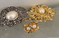 Front view showing three jewelry pieces: silver-tone oval brooch, gold-tone round brooch, gold-tone ring