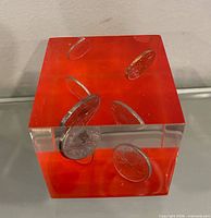 Lucite cube showing coins suspended in red and clear acrylic