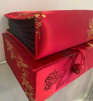 Album resting on matching storage box showing red silk cover and black pages
