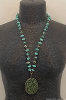 Full view of necklace on display form showing turquoise chip strand and peridot-filled pendant