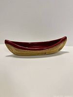 Side view showing red interior and tan exterior of ceramic canoe dish