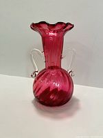 Front view of cranberry glass vase showing ruffled rim, clear handles, swirl body