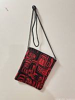 Front view of red and black Indigenous motif shoulder bag hanging on wall