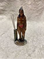 Front view of painted cast metal Indigenous man figurine with attached cylinder