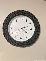 Front view of round wall clock showing dial, sub-dials and woven frame