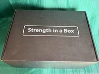 Closed black carton labelled "Strength in a Box"