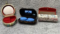 All three brocade cases open showing interiors, mirrors, lens containers and red velvet tray