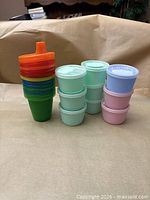 Stacked multicolour cups with spout lid beside two stacks of pastel snack containers
